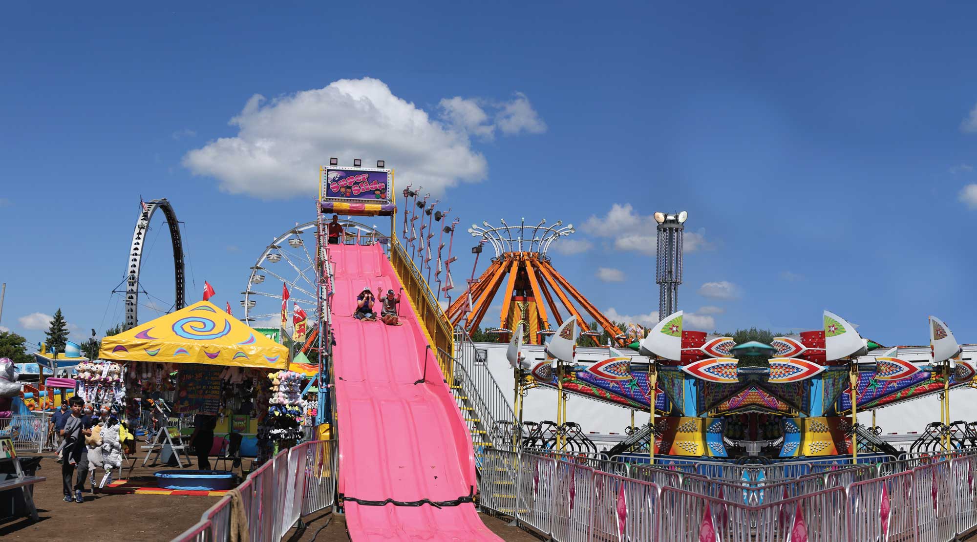 children going down pink slide at a fairground under a blue sky