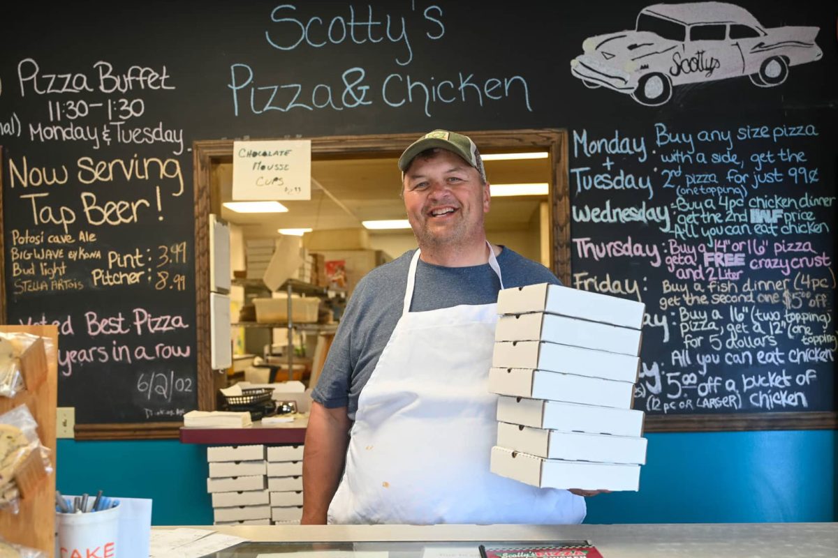 Find comfort food & cozy lodging in Marshfield this winter | Owner at Scotty’s Pizza & Chicken in Marshfield Wisconsin holding pizza boxes at counter