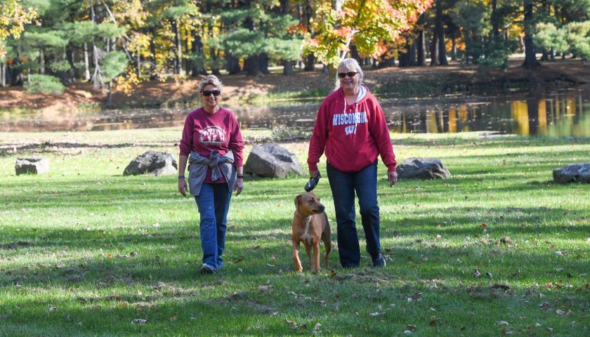 Two women walking a dog in fall at North Wood County Park near Marshfield Wisconsin