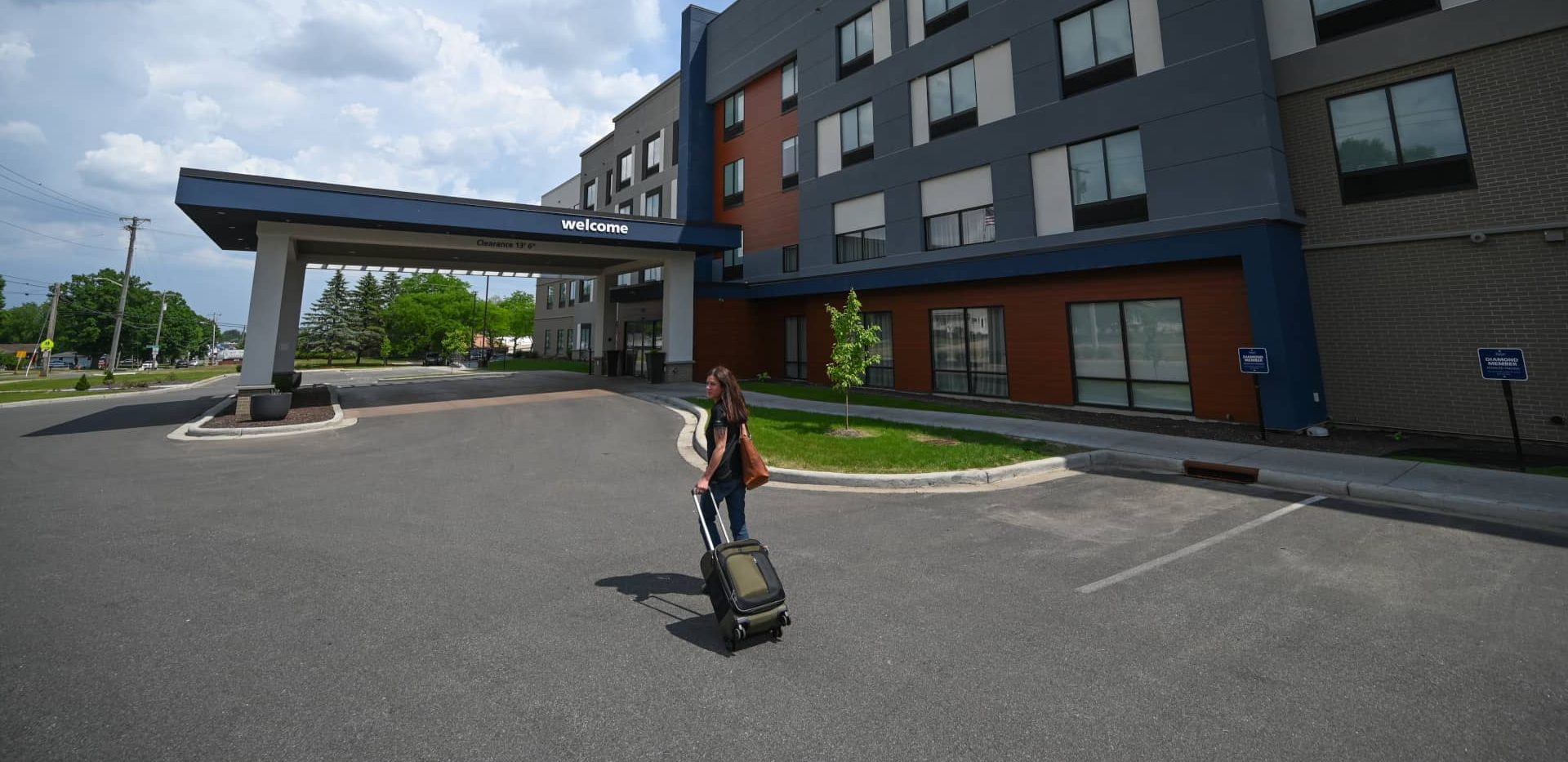 Where to stay when you’re visiting Marshfield Medical Center | Woman with rolling suitcase outside Hampton Inn & Suites in Marshfield Wisconsin